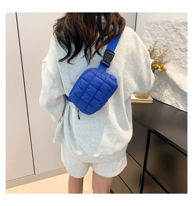 Bolso bandolera azul acolchado con textura de cuadros y hebilla negra en una modelo