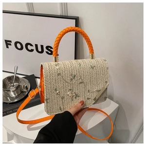 Detail of hand-woven straw bag with floral embroidery and orange leather handle