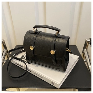 Détail d'un mini sac à main noir texturé plissé avec boucles dorées sur un livre blanc
