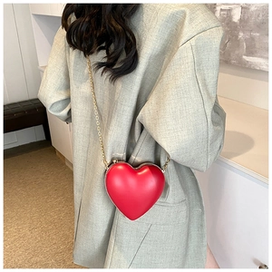 Fashionable red heart-shaped crossbody bag with gold chain strap on stylish green blazer