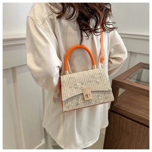 Detail of woven crossbody bag with floral embroidery and orange handle on model