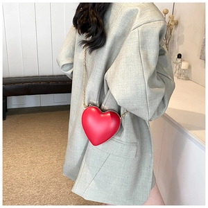 Detail of a red heart-shaped hard shell crossbody bag with a fine gold chain strap