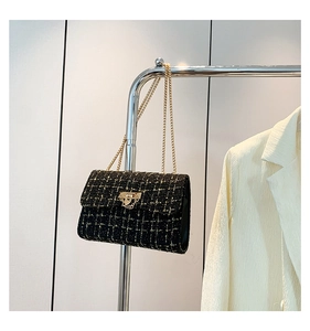 Close-up of black tweed shoulder bag with gold chain and metal buckle detail
