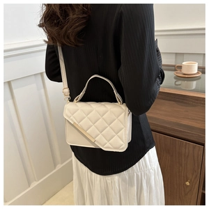 Quilted beige shoulder bag with gold metal accents worn by a model in a cozy interior