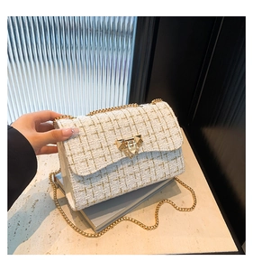 Macro shot of white tweed texture with gold thread and geometric metal lock on a chain bag