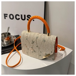Detail of floral embroidery on off-white straw handbag with orange woven handle