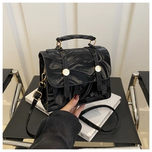 Détail d'un sac en cuir verni brillant avec finitions dorées sur une chaise rétro