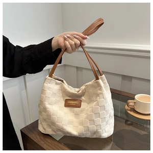 Detail of cream checkerboard tote bag featuring a leather handle and minimalist patch