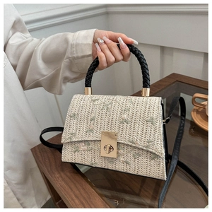 Macro detail of straw woven bag featuring floral embroidery and black braided leather handle