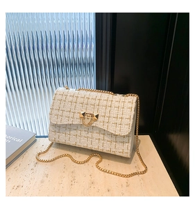 Detail of white tweed texture with gold chain strap and metallic rivet lock on small square bag