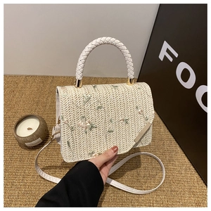 Detail of straw handbag featuring floral embroidery and woven handles in a lifestyle setting