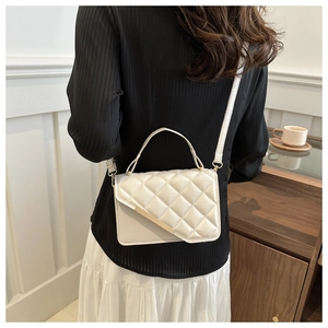 Detail of white quilted crossbody bag with gold metal trim and adjustable shoulder strap