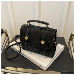 Détail d'un sac à main noir à motif marbre avec boucles dorées sur un livre
