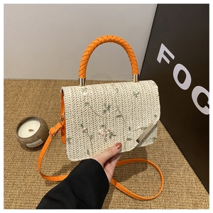 Detailed embroidery of floral patterns on beige straw handbag with orange leather handle