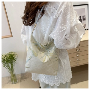 Detail of embroidered floral pattern and gold strap buckle on a beige shoulder bag