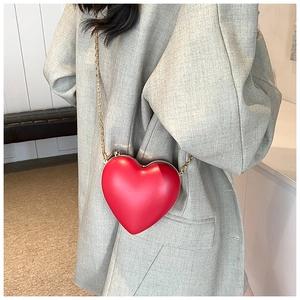 Detail of a red heart-shaped mini bag with gold chain strap worn over a grey blazer
