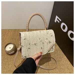 Detail of straw handbag featuring delicate floral embroidery and a woven round handle