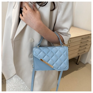 Detail of light blue quilted handbag with gold metal trim on a white blazer outfit