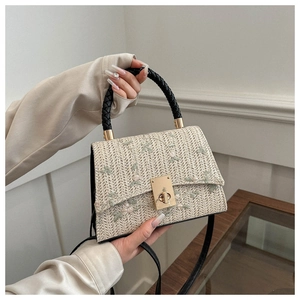 Detail of woven straw handbag featuring floral embroidery and golden metal twist lock