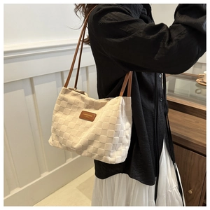 Detail of waffle-textured off-white tote bag with brown leather straps and metal plaque