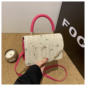 Detail of beige straw bag featuring pink floral embroidery and woven pink handle