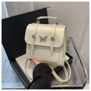 Detail of cream white faux leather bag featuring a silver butterfly metallic ornament