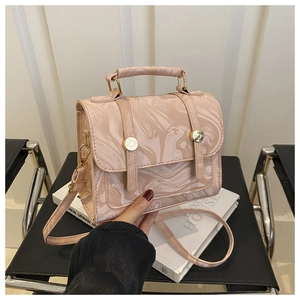 Détail du sac à main à motif marbre rose avec garnitures dorées et poignée sur chaise noire
