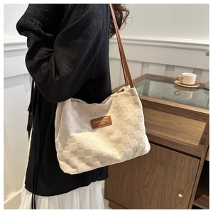 Detail of beige woven checkerboard tote bag with brown leather strap worn by a model