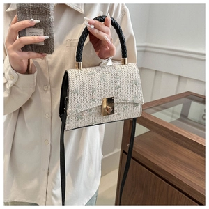 Detailed shot of beige woven handbag with floral embroidery and golden twist lock