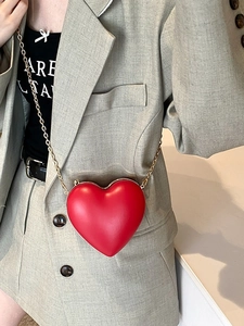 Fashionable red heart shaped crossbody bag with gold chain strap on a stylish model