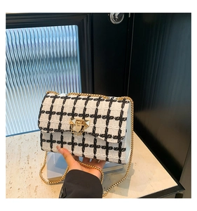 Close-up of black and white tweed texture with gold chain and clasp on the shoulder bag