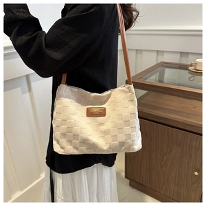 Detail of checkered woven tote bag with brown leather shoulder strap and fashion label