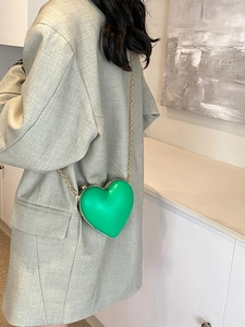 Fashionable green heart-shaped crossbody bag with gold chain worn on a grey blazer