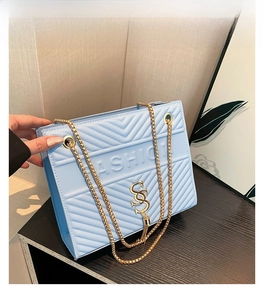 Detail of light blue quilted leather bag with gold chain and metal logo on wood surface