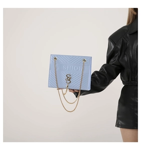 Detail of light blue quilted crossbody bag featuring gold chain and tassel ornament