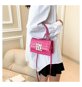 Detailed view of pink croc-embossed handbag featuring a silver gothic letter metal buckle