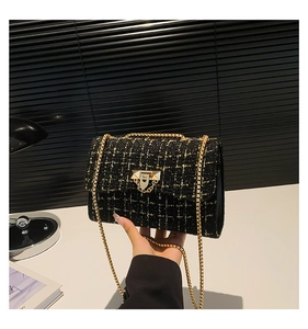 Close-up of black tweed shoulder bag with gold chain strap and metallic lock buckle