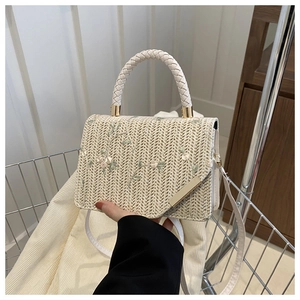 Detail of cream straw handbag featuring delicate floral embroidery and metal clasp closure