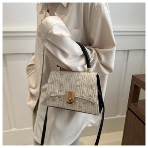 Detail of retro straw crossbody bag featuring floral embroidery and a black woven handle