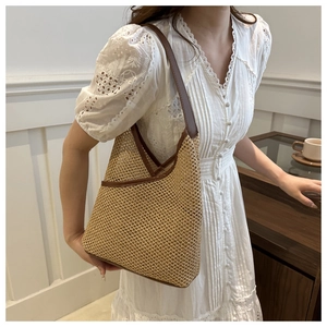 Handwoven straw bucket bag with dark brown leather shoulder strap in a stylish home setting
