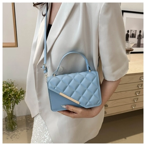 Detailed view of light blue quilted square bag with gold hardware on a white blazer