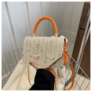 Detail of straw woven bag featuring floral embroidery and orange woven handle in hand