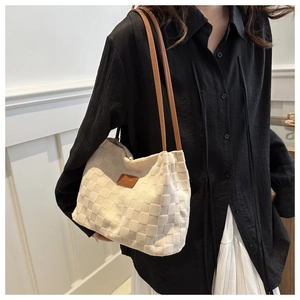 Detail of cream woven tote bag with brown leather straps worn on shoulder by model