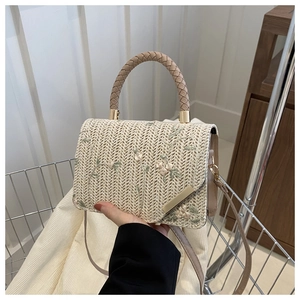 Detailed close-up of woven straw bag with green vine embroidery and sturdy handle