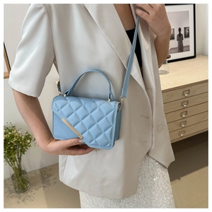 Detail of light blue quilted leather handbag with gold bar accent and curved top handle