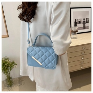 Side view of light blue quilted crossbody bag worn by a model in a modern home setting