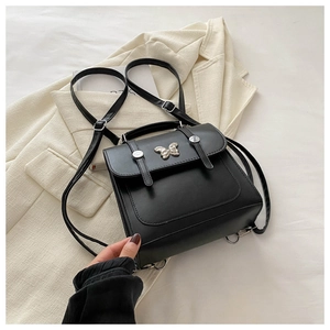 Detail of a mini black leather backpack featuring a silver butterfly buckle on a suit