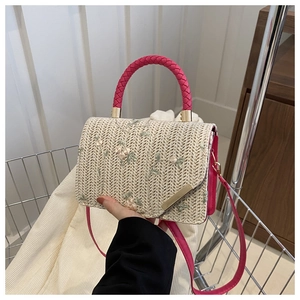 Detail of floral embroidery on beige woven handbag with pink handles and golden hardware