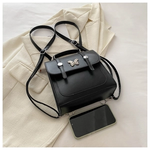 Detail of black leather butterfly backpack next to smartphone for size comparison