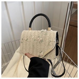 Close-up of a woven straw handbag featuring delicate floral embroidery and a gold buckle